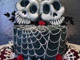 a black and white spiderweb wedding cake with red blooms and large skull toppers plus black leaves