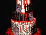 a black, red and white wedding cake with bloody dripping, patterns, gravestones, fances and a gravestone topper for a Halloween wedding