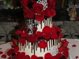 a white wedding cake with chocolate drip, red petals, red roses, spiders, spiderwebs, a dragon ball on top for a Halloween wedding