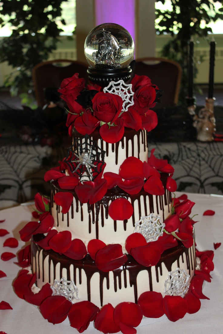 A white wedding cake with chocolate drip, red petals, red roses, spiders, spiderwebs, a dragon ball on top for a Halloween wedding