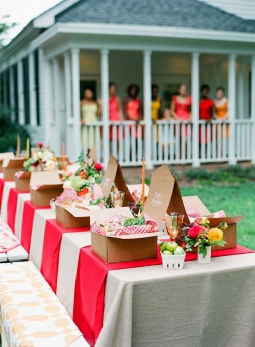 a bright rustic picnic with red and white textiles, bright blooms and apples and boxes with food