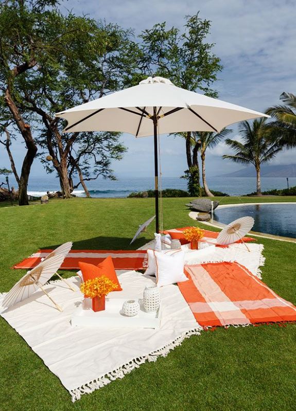 A bright picnic setting with colorful blankets, umbrellas and bright blooms by the pool