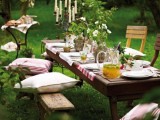 a garden picnic setting with white blooms and greenery, with candles, benches and chairs with pillows