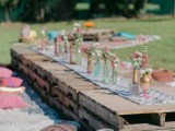 a bright boho picnic setting with a low pallet table, bright blooms, blankets and pillows for a rehearsal dinner