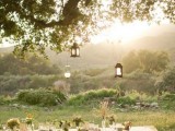 a simple summer picnic with lanterns, trestle wooden furniture, a lace tablecloth, some wildflowers