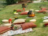a bright and very simple picnic setting with bright and plaid pillows, blankets, candle lanterns and a fire pit