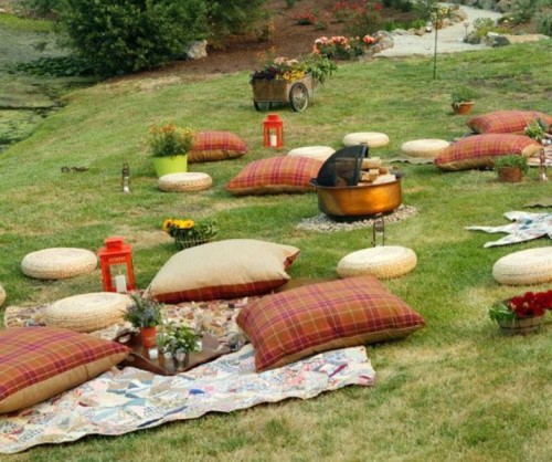 a bright and very simple picnic setting with bright and plaid pillows, blankets, candle lanterns and a fire pit