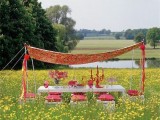 a super bright boho picnic on a lawn, with red pillows and a red printed cover over the table