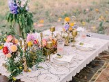 a bright summer boho picnic with a low table covered with doilies, bright blooms and greenery and gold candleholders