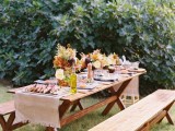 a simple picnic setting with a trestle furniture set, some bold blooms and fall leaves and delicious food