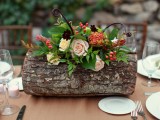 a fall woodland wedding centerpiece of a tree stump, bold and blush blooms, greenery, berries is a creative and cool idea