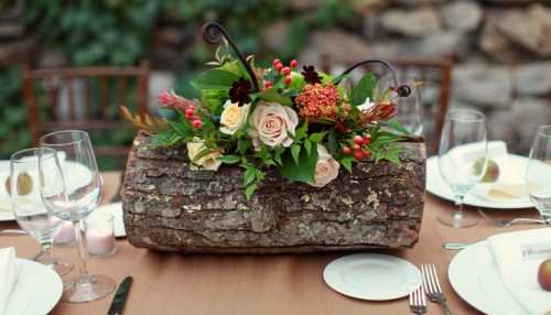 a fall woodland wedding centerpiece of a tree stump, bold and blush blooms, greenery, berries is a creative and cool idea