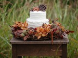 a textural white wedding cake topped with blooms and lotus slices, surrounded with bold fall leaves and flowers is ideal for a fall woodland wedding