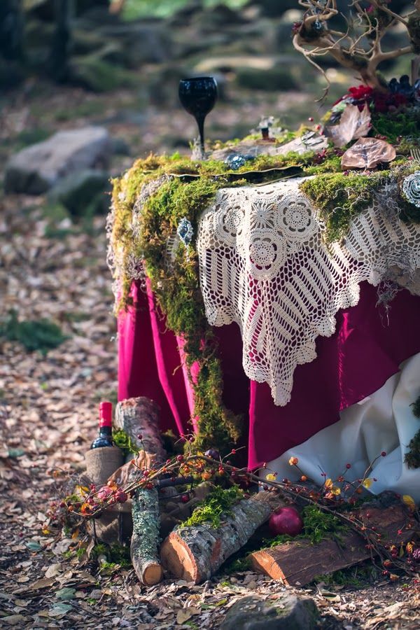 A fairy tale like woodland wedding reception with layered tablecloths and a moss runner, branches, bold blooms and firewood and berries at the table