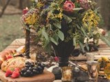a jewel-tone wedding reception table with greenery, bold blooms, thistles, a small cheese board and gold touches
