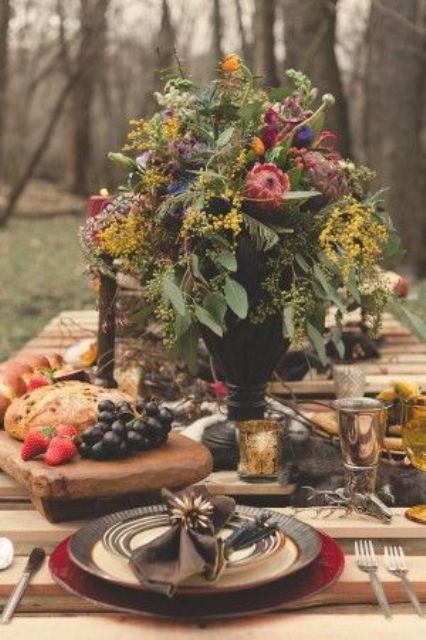 a jewel-tone wedding reception table with greenery, bold blooms, thistles, a small cheese board and gold touches