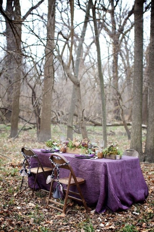a moody fall woodland wedding tablescape with a purple tablecloth, candles, some flowers and greenery is a statement solution for a woodland wedding