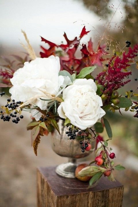 a bold fall woodland wedding centerpiece of berries, white flowers, bright leaves and branches