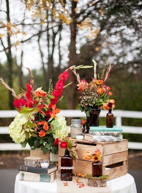 bold fall woodland wedding decor of brigth red blooms, greenery, dark vases, books and crates plus candles is a chic idea