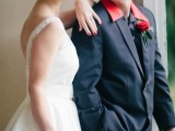 a groom wearing a black suit and a red shirt with a red rose boutonniere and a bride rocking red touches, too