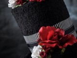 a black wedding cake with hot red and white flowers plus ribbons
