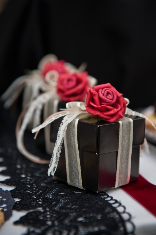 black boxes with white ribbons and red roses on top to pack wedding guest favors