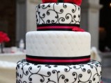 a black and white wedding cake with various patterns and touches of red and red roses