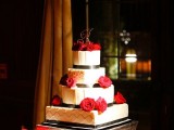 a white wedding cake decorated with black ribbons and red roses on top