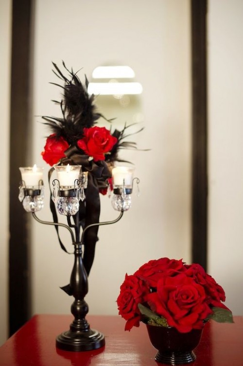 a black and red wedding centerpiece with candles, roses and feathers