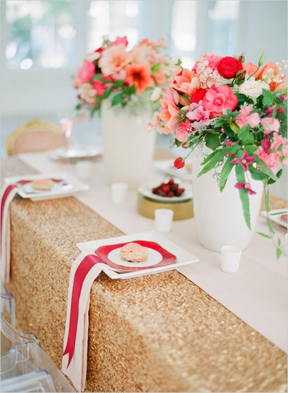 A gold sequin tablecloth, striped napkins, a printed plate and bright red and pink florals for centerpieces