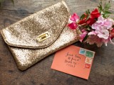 a gold sequin clutch, a coral envelope and a wedding bouquet of pink and red blooms and greenery