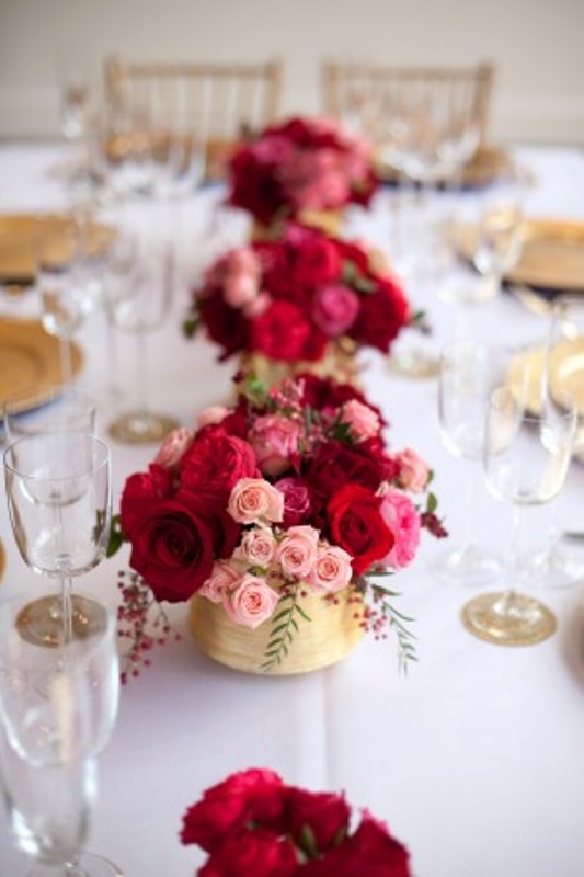 Red and pink floral centerpieces with berries in gold vases are amazing to add color to your tables