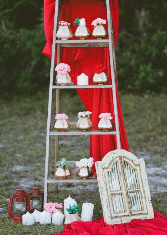 A ladder with gold vases and pink and red blooms plus some red fabric for glam and bold wedding decor