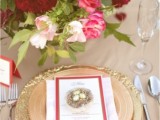 a wedding centerpiece of burgundy, pink and blush blooms and gold plates and placemats for a glam and chic look