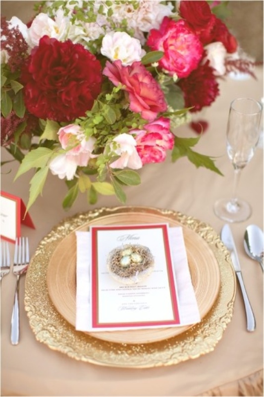 A wedding centerpiece of burgundy, pink and blush blooms and gold plates and placemats for a glam and chic look