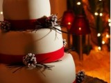 a white wedding cake decorated with red ribbon and snowy pinecones plus some evergreens is a lovely idea for a winter wedding