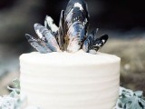 a white wedding cake topped with mussel shells looks very relaxed, beach-like and boho