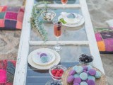 a boho beach picnic setting with a vintage window as a tabletop, colorful pillows, macarons and berries