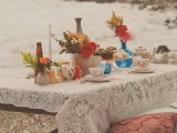 a boho beach wedding picnic setting with a low table, a lace tablecloth, colorful blooms and greenery plus pillows