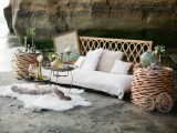a boho beach lounge with a rattan sofa and side tables, faux fur, blooms and artworks