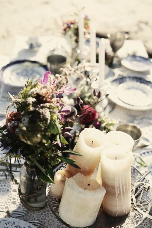a relaxed boho beach wedding reception table with bright blooms, candles and printed plates and a tablecloth