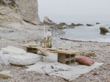 a simple boho beach reception with blankets and pillows, a concrete and wood table and candles