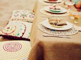 a bright boho beach setting with an ocher tablecloth, colorful pillows and plates and bright glasses
