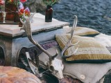 a moody boho beach setting with a low table, pillows, a leather pouf, bright blooms and a skull