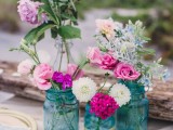 a bright boho beach wedding centerpiece with blue jars and bright blooms and driftwood with candles
