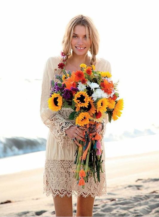 a simple and neutral boho beach wedding dress with a lace trim on the skirt and sleeves plus a bright bouquet
