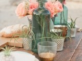 a boho beach wedding centerpiece with candle lanterns, air plants in holders, coral pink blooms and greenery in turquoise bottles