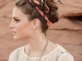 a braided updo with a coral ribbon and some feathers is a bold and bright idea for a boho wedding