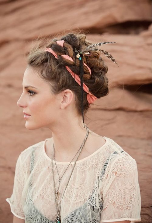 a braided updo with a coral ribbon and some feathers is a bold and bright idea for a boho wedding