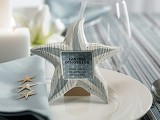 a light blue and white place setting with a starfish name holder, a striped tablecloth, a light blue napkin and candles